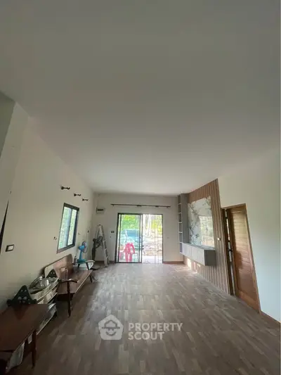 Spacious living room with wooden flooring and large windows for natural light.