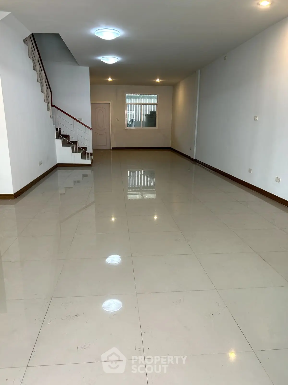 Spacious empty living room with glossy tiled floors and staircase, ideal for customization.
