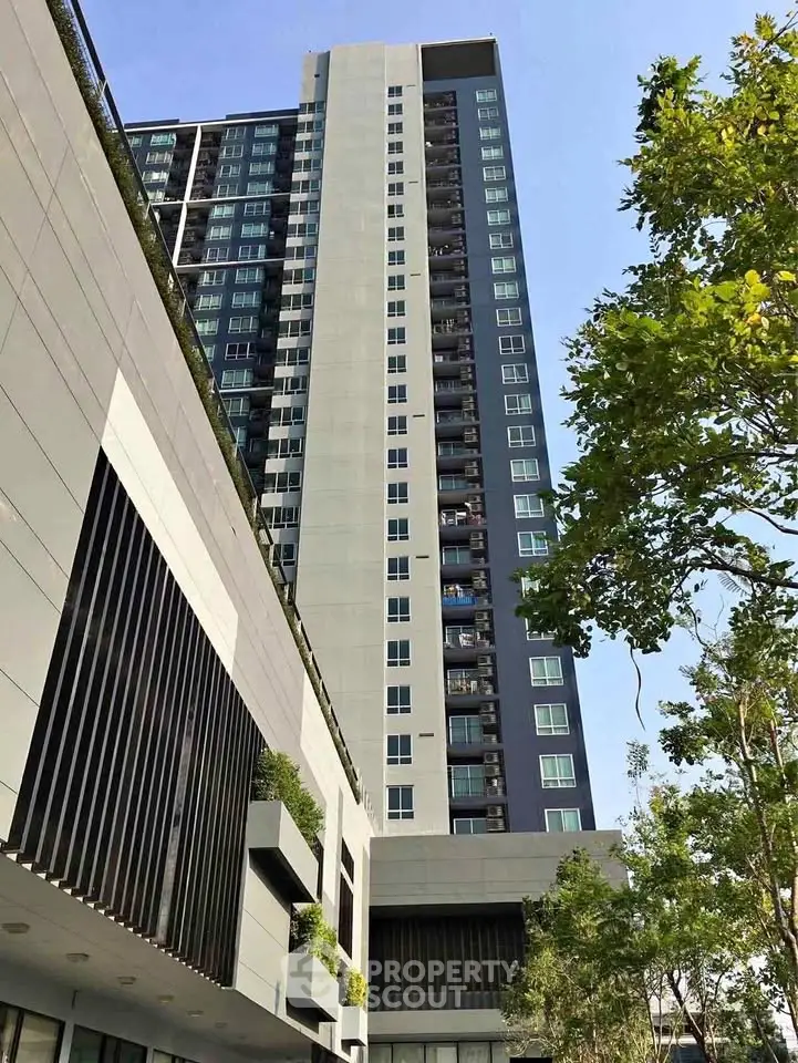 Modern high-rise building with sleek design and lush greenery in urban setting.