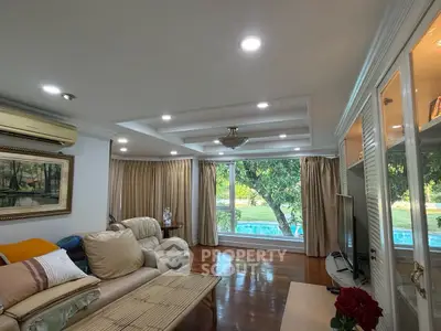 Spacious living room with large windows offering a serene garden view, elegant furnishings, and cozy ambiance.