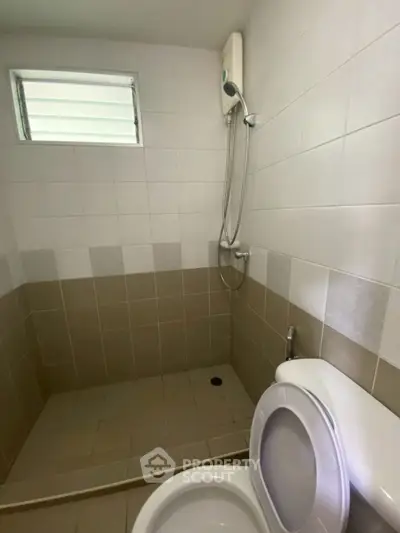 Compact bathroom with shower and toilet, featuring neutral tile design.