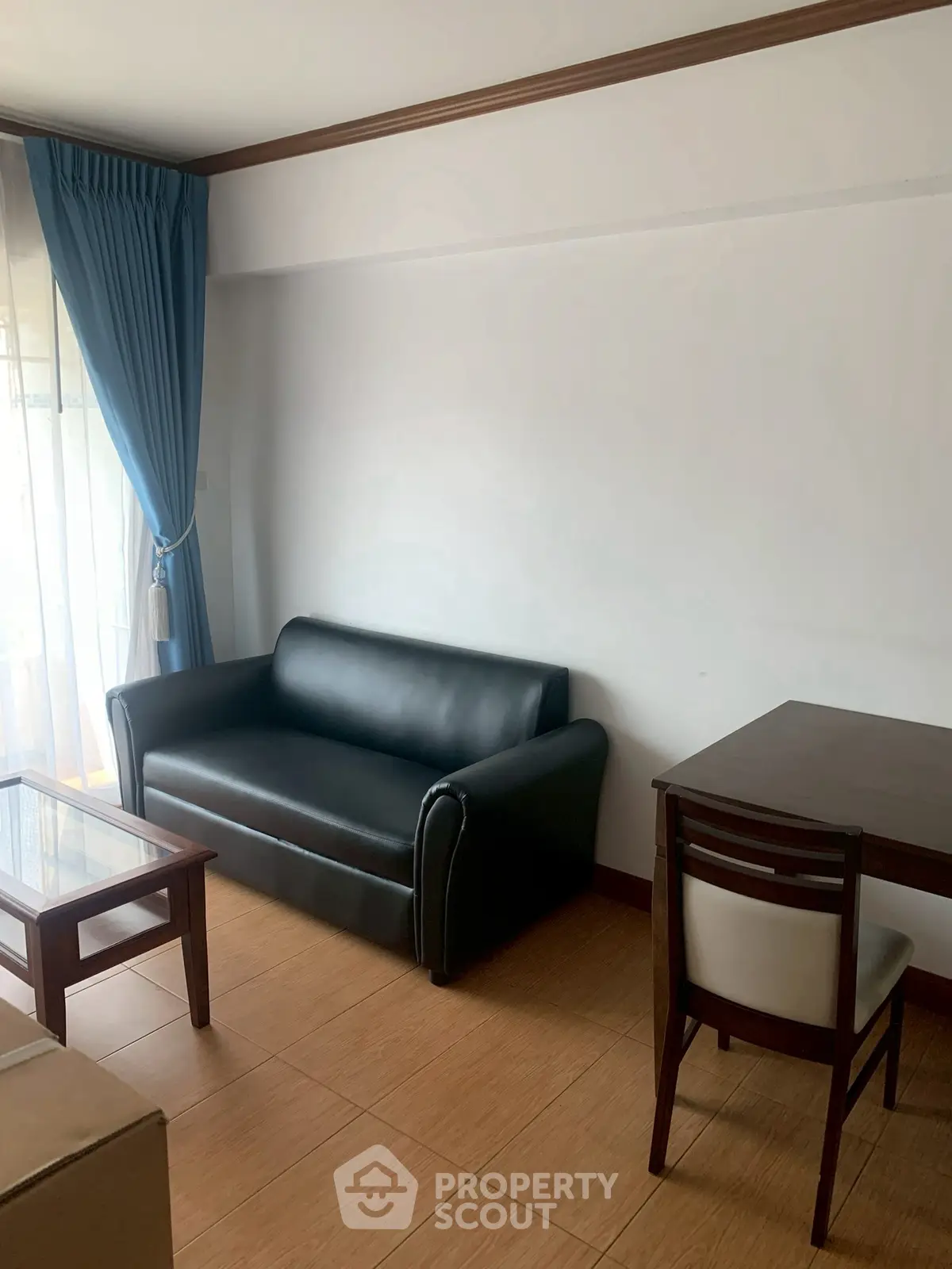 Cozy living room with black sofa and wooden furniture, natural light from large window.