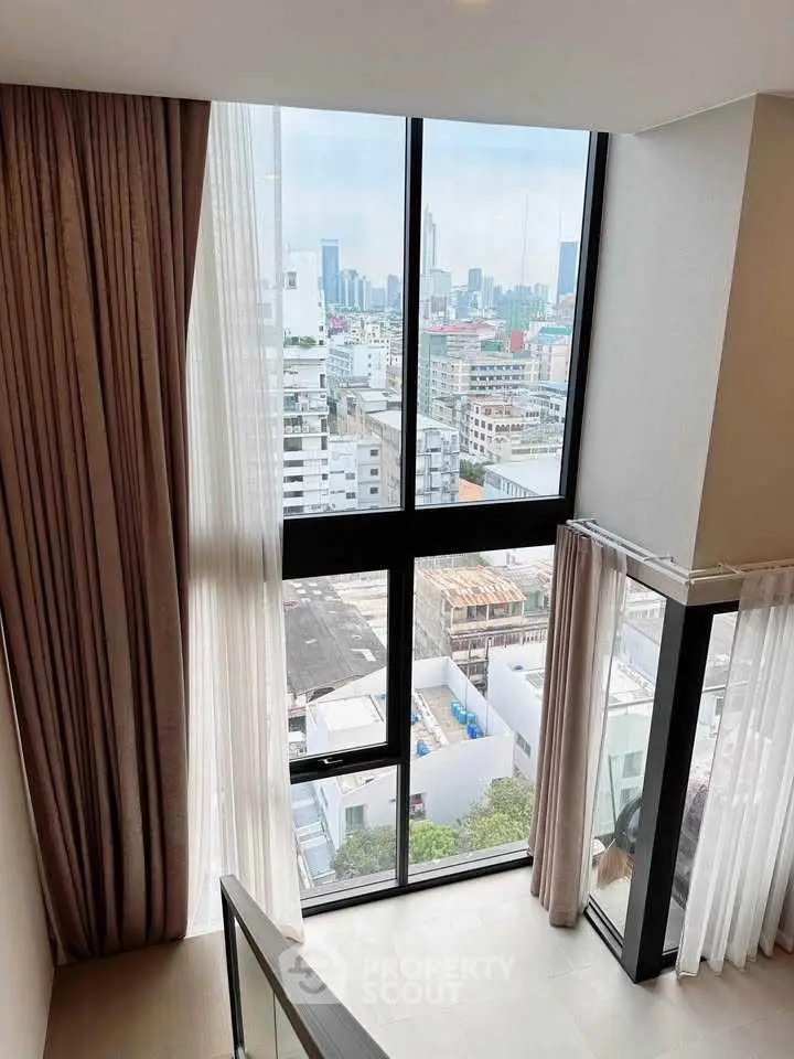 Stunning city view from modern high-rise apartment with floor-to-ceiling windows and elegant curtains.