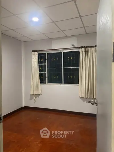 Spacious empty room with wooden flooring and large window, ideal for customization.