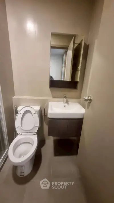 Modern bathroom with sleek fixtures and neutral tones, featuring a toilet and a compact sink.