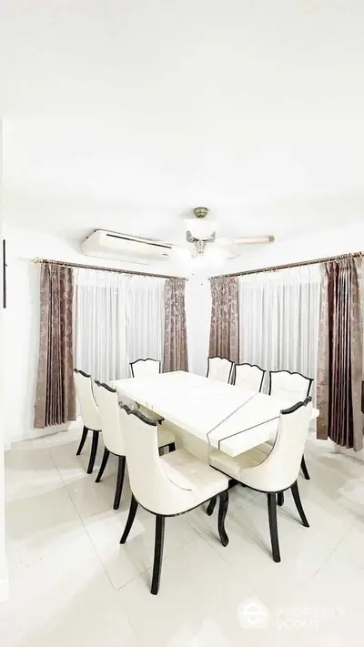 Elegant dining room with modern white table and chairs, surrounded by large windows and curtains.