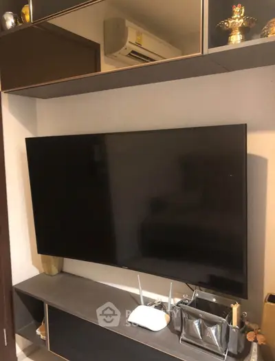 Modern living room with wall-mounted TV and sleek storage unit, featuring contemporary decor and air conditioning.