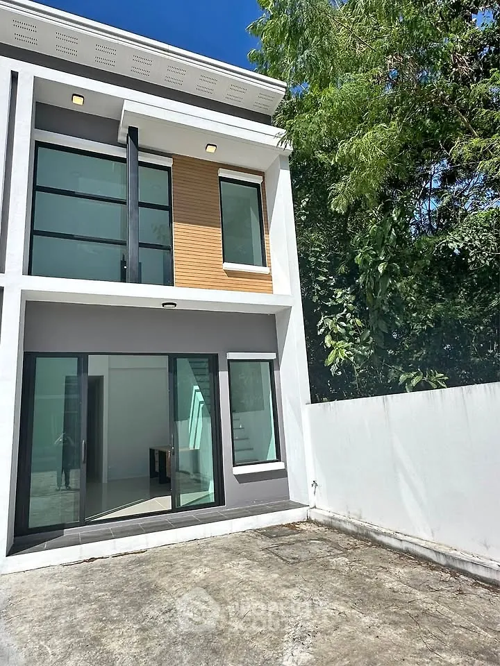 Modern two-story house with large windows and private outdoor space, surrounded by lush greenery.