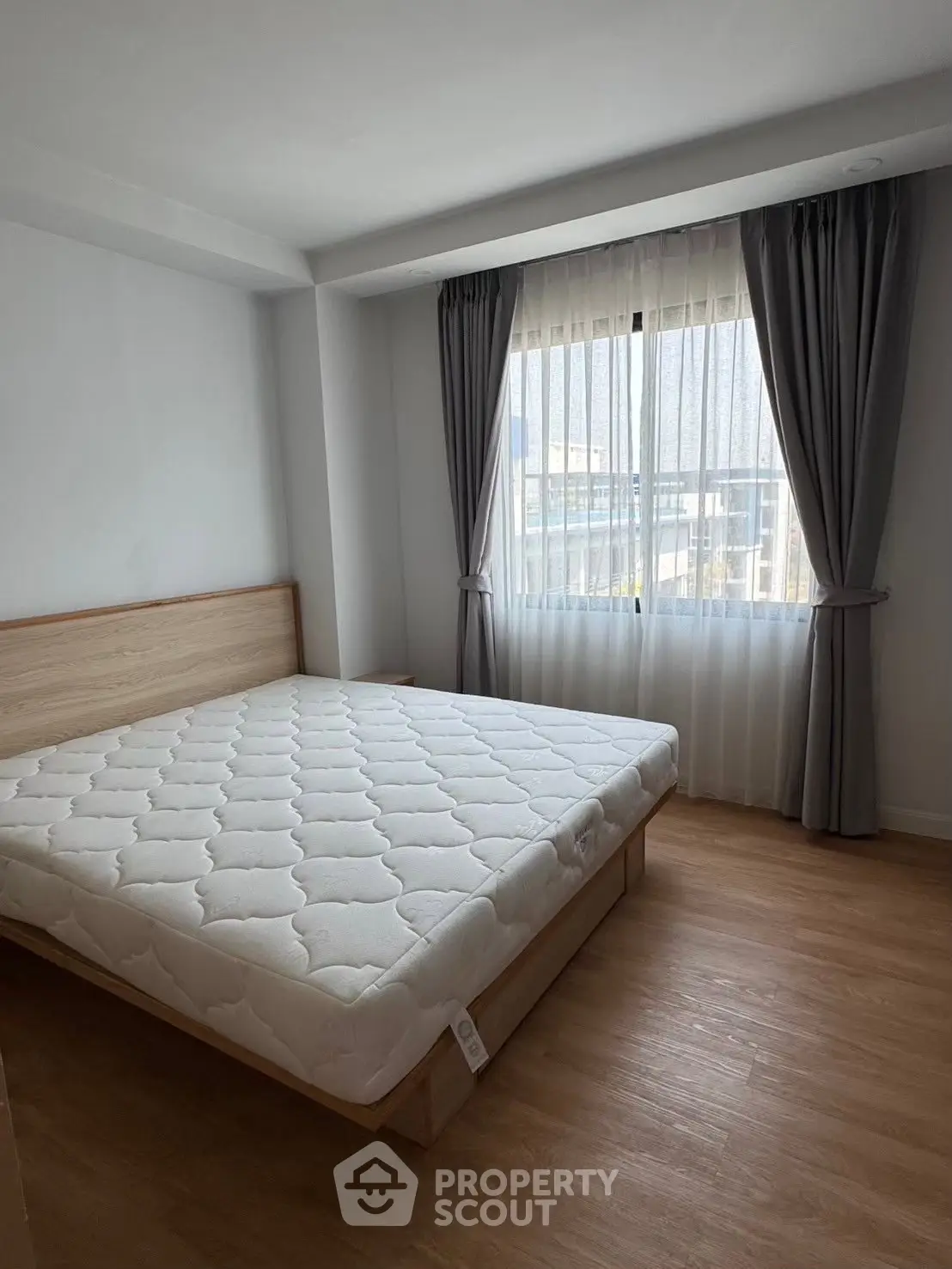 Spacious bedroom with large window and wooden flooring in modern apartment.