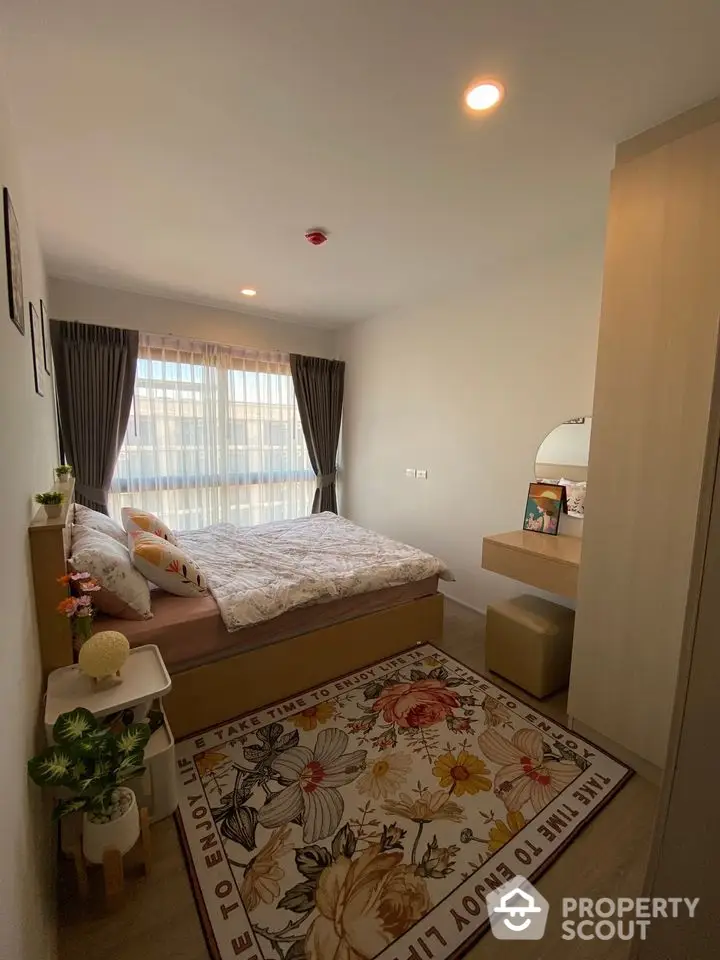 Cozy bedroom with large window and floral rug, perfect for relaxation and comfort.