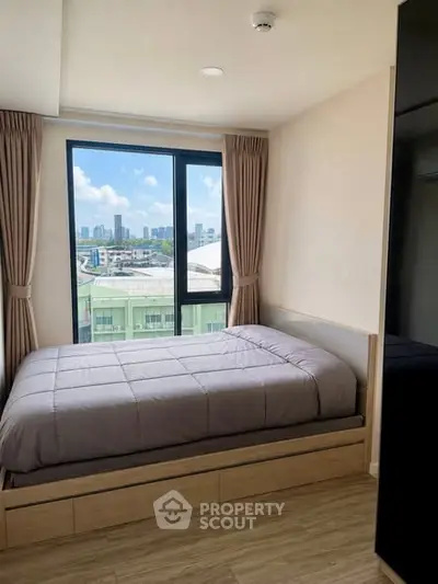 Cozy bedroom with city view, featuring a comfortable bed and large window for natural light.