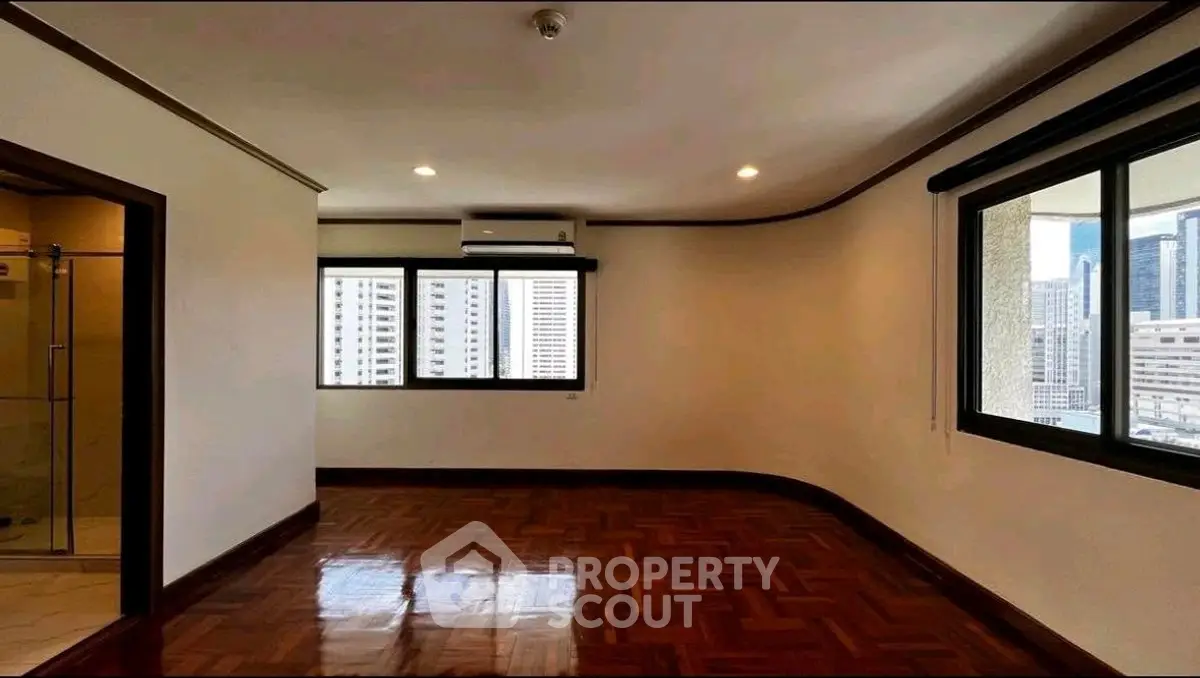 Spacious empty room with polished wooden floors and city view windows