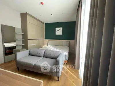 Modern bedroom with stylish decor and natural light, featuring a cozy gray sofa and sleek wooden flooring.