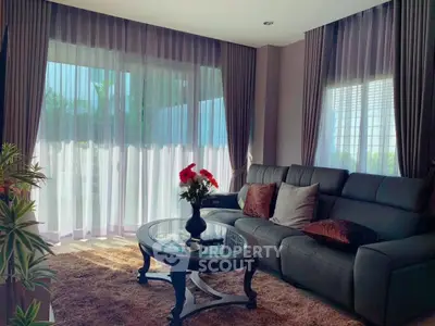 Elegant living room with plush sofa, glass coffee table, and large windows with sheer curtains.