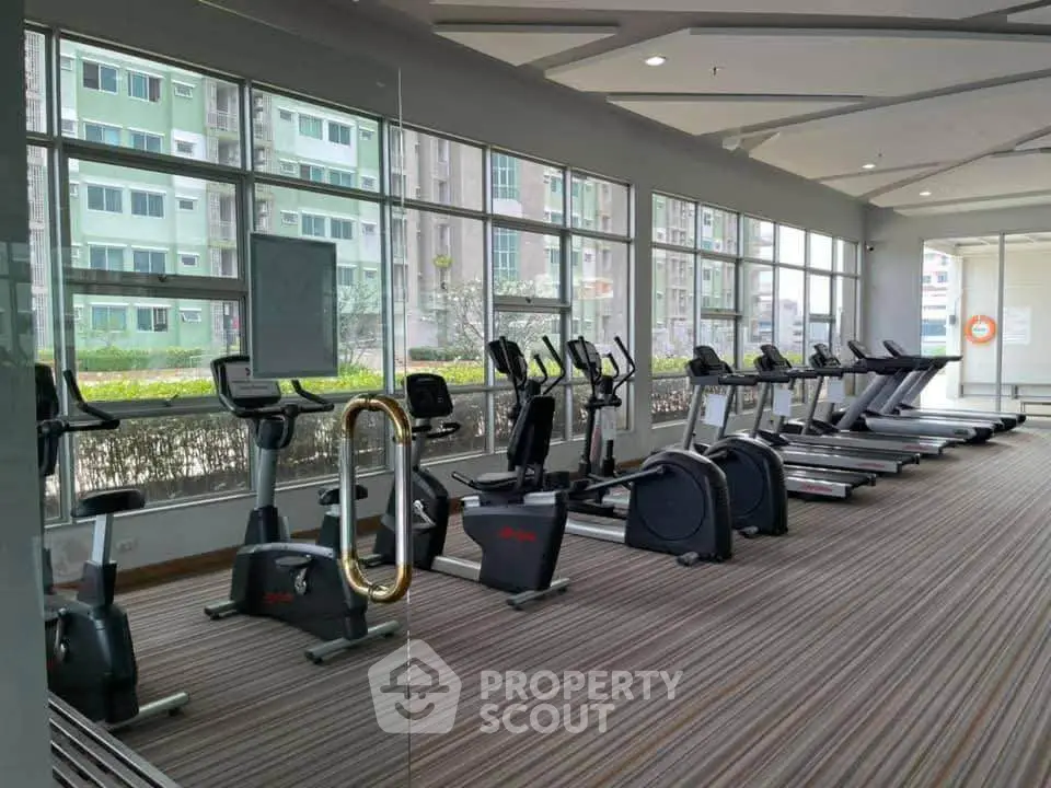 Modern gym with cardio equipment and large windows in a residential building.