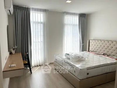 Modern bedroom with large windows, stylish bed, and sleek workspace in a bright apartment.