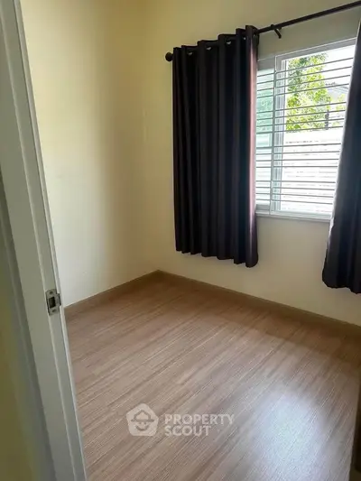 Cozy small bedroom with wooden flooring and dark curtains, perfect for minimalist living.