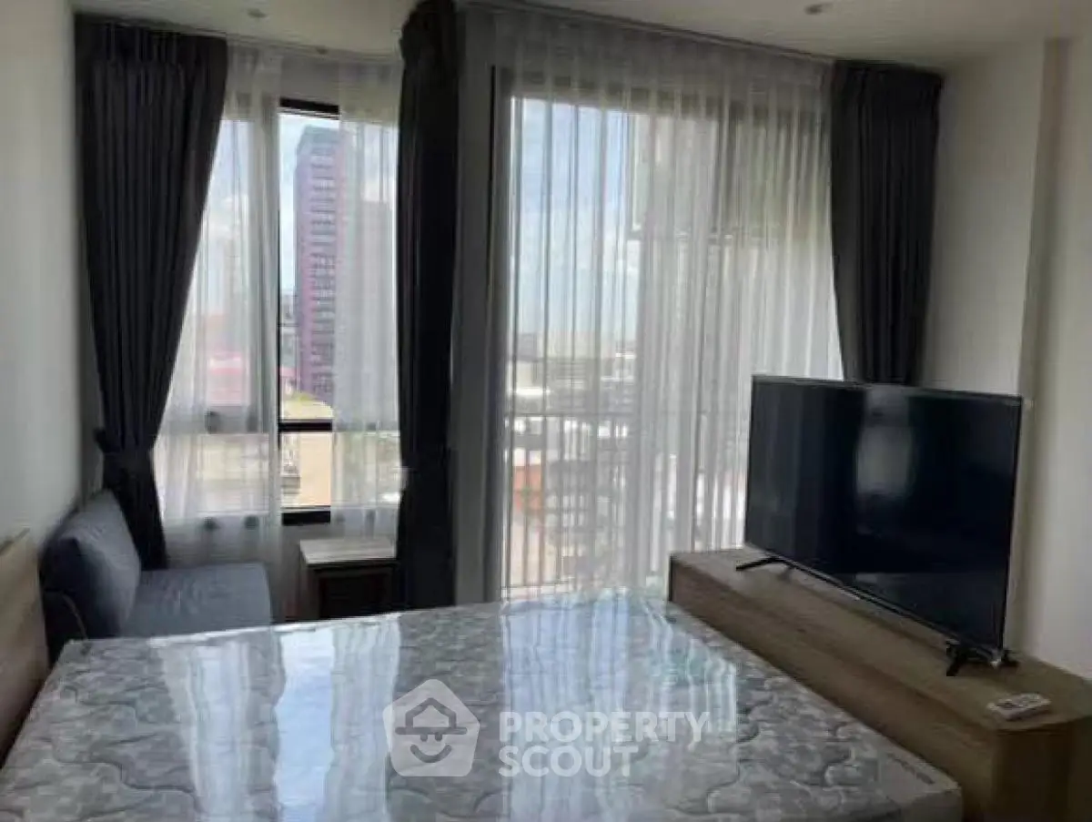 Modern bedroom with large windows and city view, featuring a TV and stylish curtains.