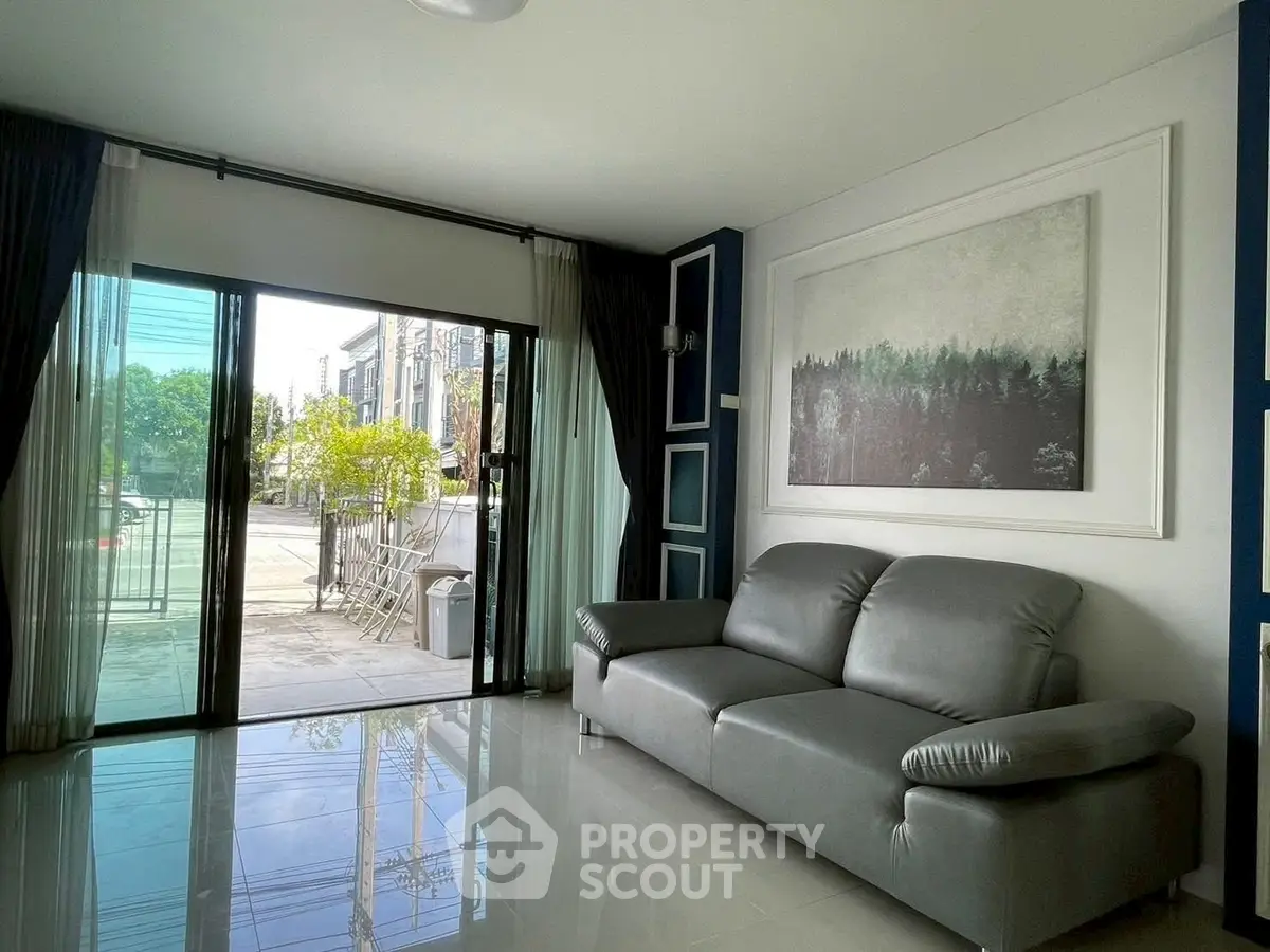 Modern living room with sleek gray sofa and large window offering natural light and outdoor view.