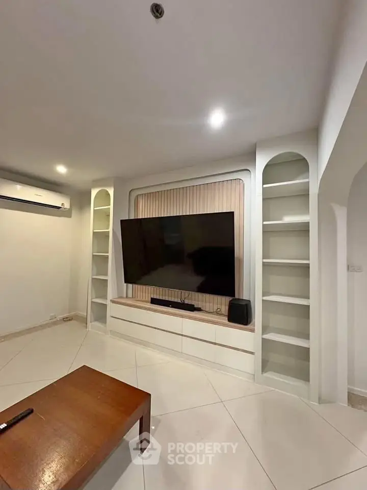 Spacious living room with modern TV setup and built-in shelves, perfect for entertainment.