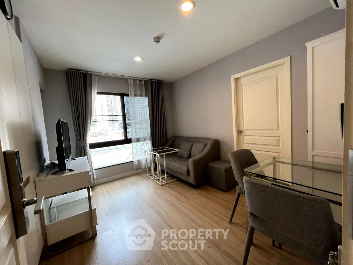 Modern living room with sleek furniture and large window offering city view.