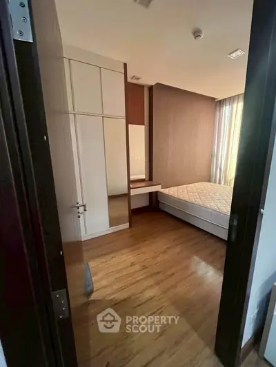 Cozy bedroom with wooden flooring and ample natural light, featuring a built-in wardrobe and a comfortable bed.