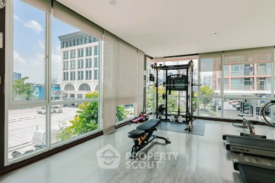 Spacious gym with modern equipment and large windows offering city views.