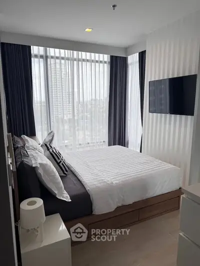 Modern bedroom with large windows and city view, featuring a wall-mounted TV and stylish decor.