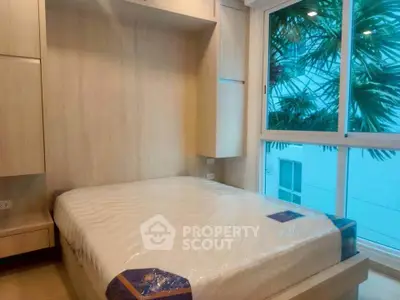 Cozy bedroom with large window and built-in storage, offering a serene view of lush greenery.