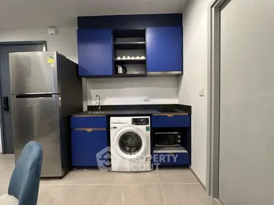Modern kitchen with blue cabinets, washing machine, and stainless steel fridge.