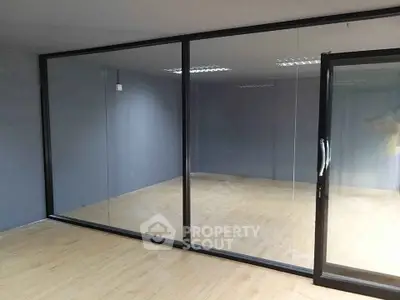 Spacious modern room with glass partition and wooden flooring, ideal for office or studio setup.