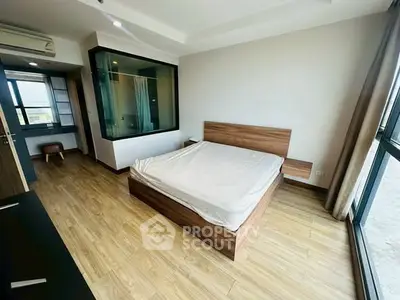 Spacious modern bedroom with wooden flooring and large windows for natural light.