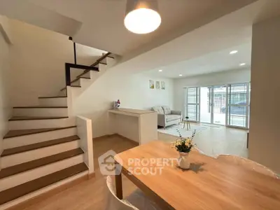 Modern open-plan living room with staircase and dining area, featuring natural light and contemporary decor.