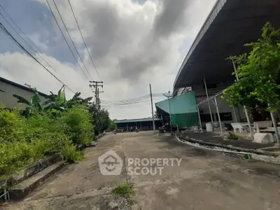 Expansive industrial property with open paved area and lush greenery, perfect for commercial use.