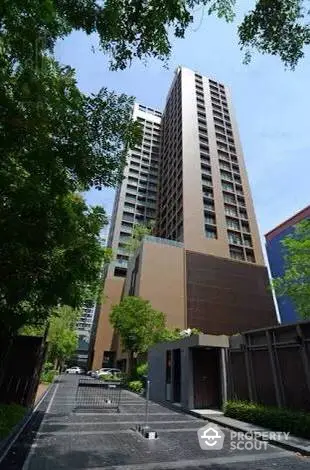 Majestic high-rise residential building towering over a serene tree-lined street, offering a blend of urban living and tranquil green spaces.