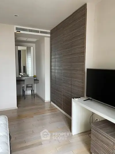Modern bedroom with sleek wooden paneling and flat-screen TV, featuring a stylish vanity area.