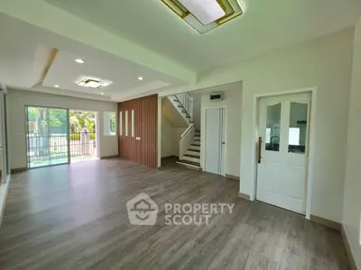 Spacious modern living room with wooden flooring and large windows overlooking greenery.