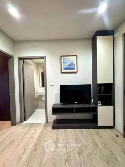 Modern living room with sleek TV unit and wooden flooring, adjacent to a bathroom entrance.