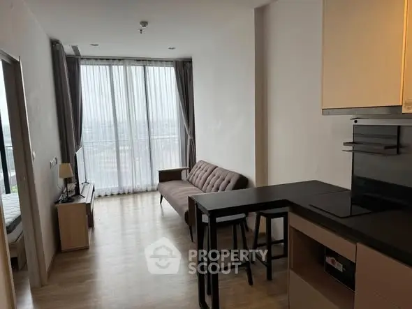 Modern living room with open kitchen and large windows offering natural light.