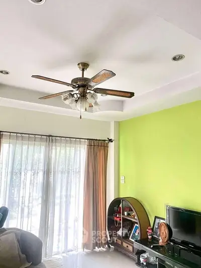 Bright living room with ceiling fan, green accent wall, and modern entertainment setup.