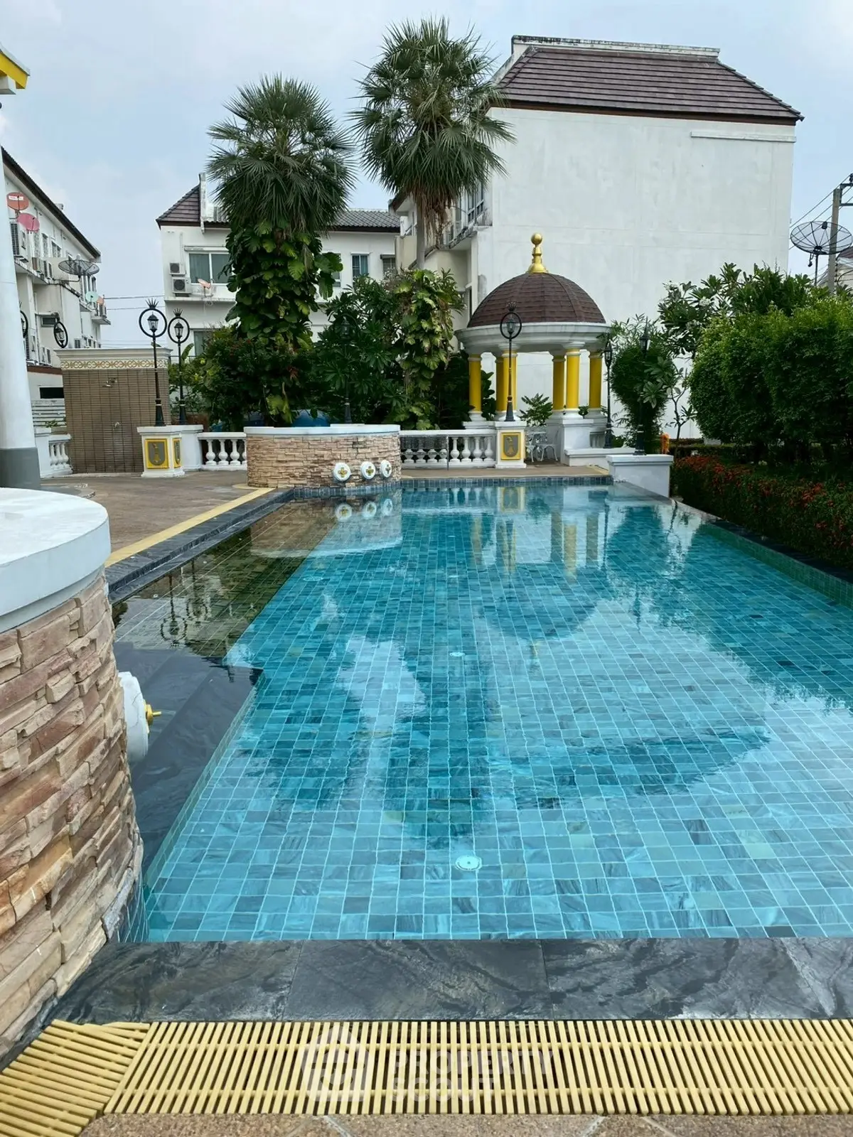Luxurious outdoor pool with elegant gazebo and lush greenery in a serene residential setting.