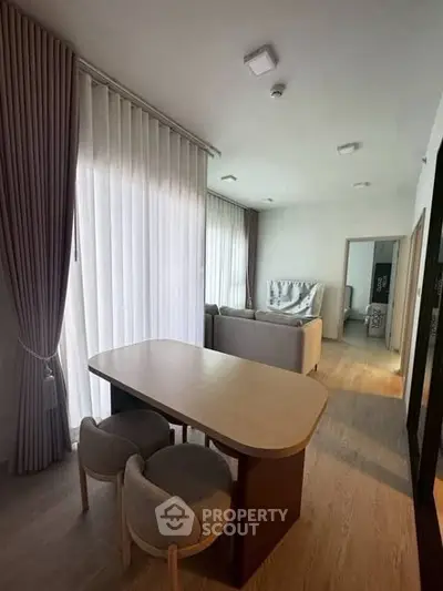 Modern living room with elegant dining area and stylish furniture, featuring floor-to-ceiling curtains and wooden flooring.