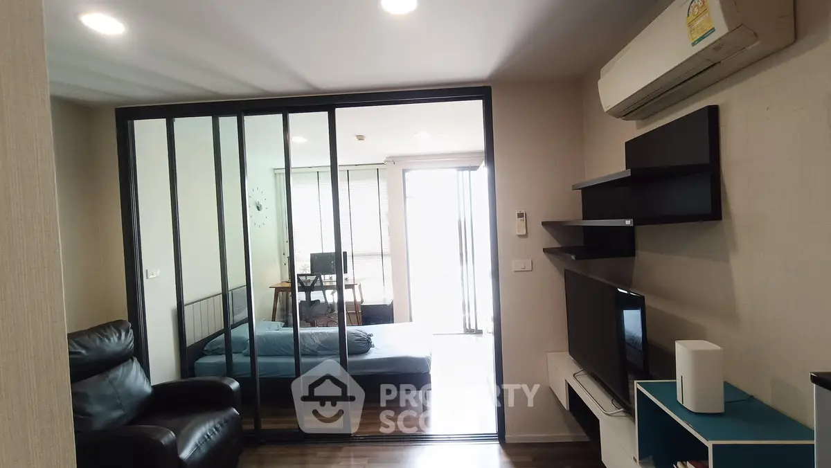Modern living room with sliding glass doors leading to a cozy bedroom, featuring sleek furniture and air conditioning.