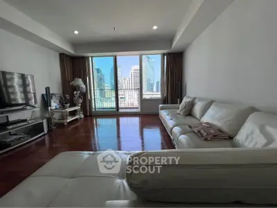 Spacious living room with city view, featuring modern white leather sofas and large windows.