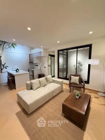 Modern open-layout living room with stylish furniture and kitchen area, featuring large windows and elegant decor.