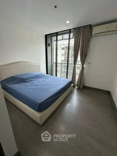 Modern bedroom with large window and city view, featuring a stylish bed and sleek flooring.