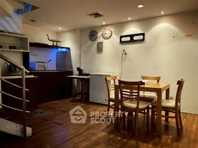 Cozy dining area with wooden flooring and modern lighting, featuring a compact kitchen corner with appliances.