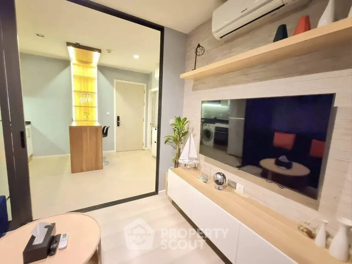 Modern living room with sleek TV setup and open kitchen view, featuring stylish decor and ample lighting.