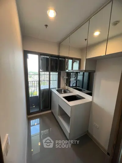 Modern kitchen with sleek design and balcony view, featuring mirrored cabinets and compact layout.