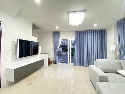 Modern living room with sleek design, large TV, and elegant curtains leading to outdoor space.